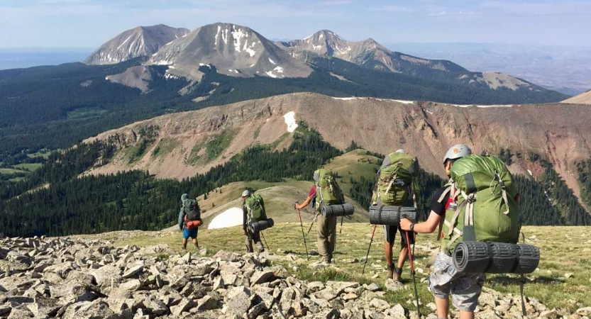 A group of backpackers hike along a rocky trail overlooking a mountainous landscape